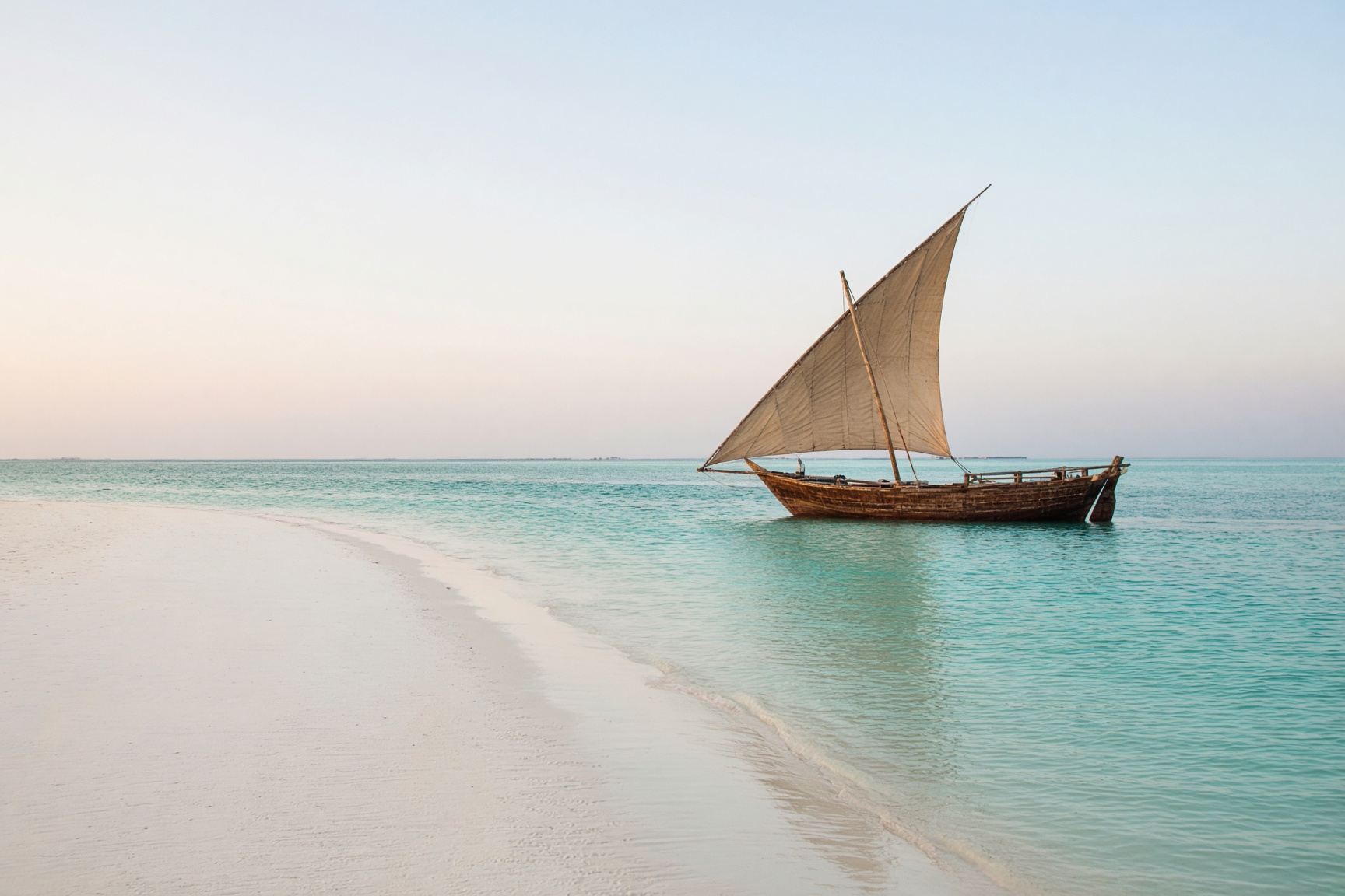 A dhow beside a white sandbank in turquoise water